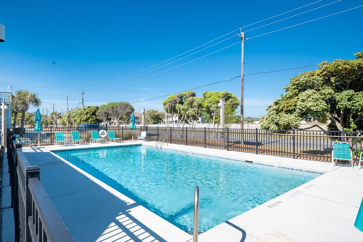 A vibrant outdoor swimming pool surrounded by lounge chairs and umbrellas, inviting guests to swim, sunbathe, and relax. The setting is perfect for family fun, with ample space for gatherings and poolside activities under the sun.