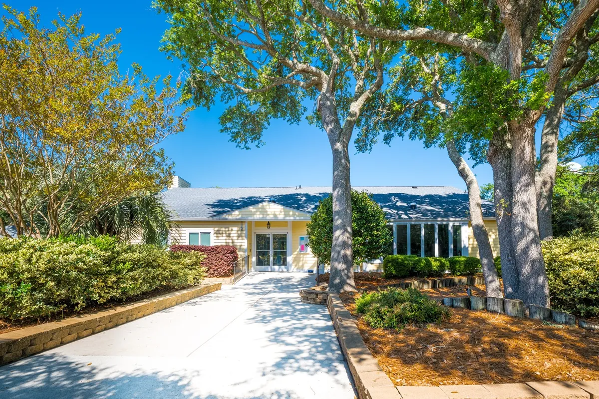 The main entrance to the property is nestled among large shade trees and landscaped gardens. The scene exudes a warm, inviting mood, with space for gathering or relaxing outdoors, suggesting a seamless connection between the home and its natural surroundings.