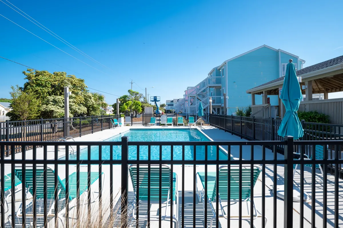 A sparkling swimming pool surrounded by comfortable lounge chairs, umbrellas, and lush greenery provides a relaxed, social setting perfect for groups. The inviting pool area is ideal for sunbathing, swimming, and enjoying time with friends, reflecting the fun-loving island vibe described in the section.