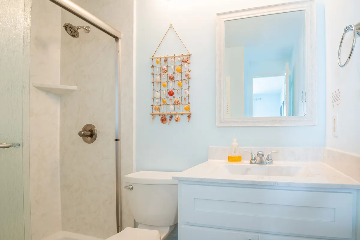A modern, spa-inspired bathroom featuring a walk-in shower, a sleek sink with mirror, and a decorative wall hanging. The space is softly lit and styled with calming tones, evoking a sense of peace and relaxation.